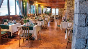 Un restaurante con varias mesas dispuestas para comer, vigas de madera en el techo y grandes ventanales con cortinas.