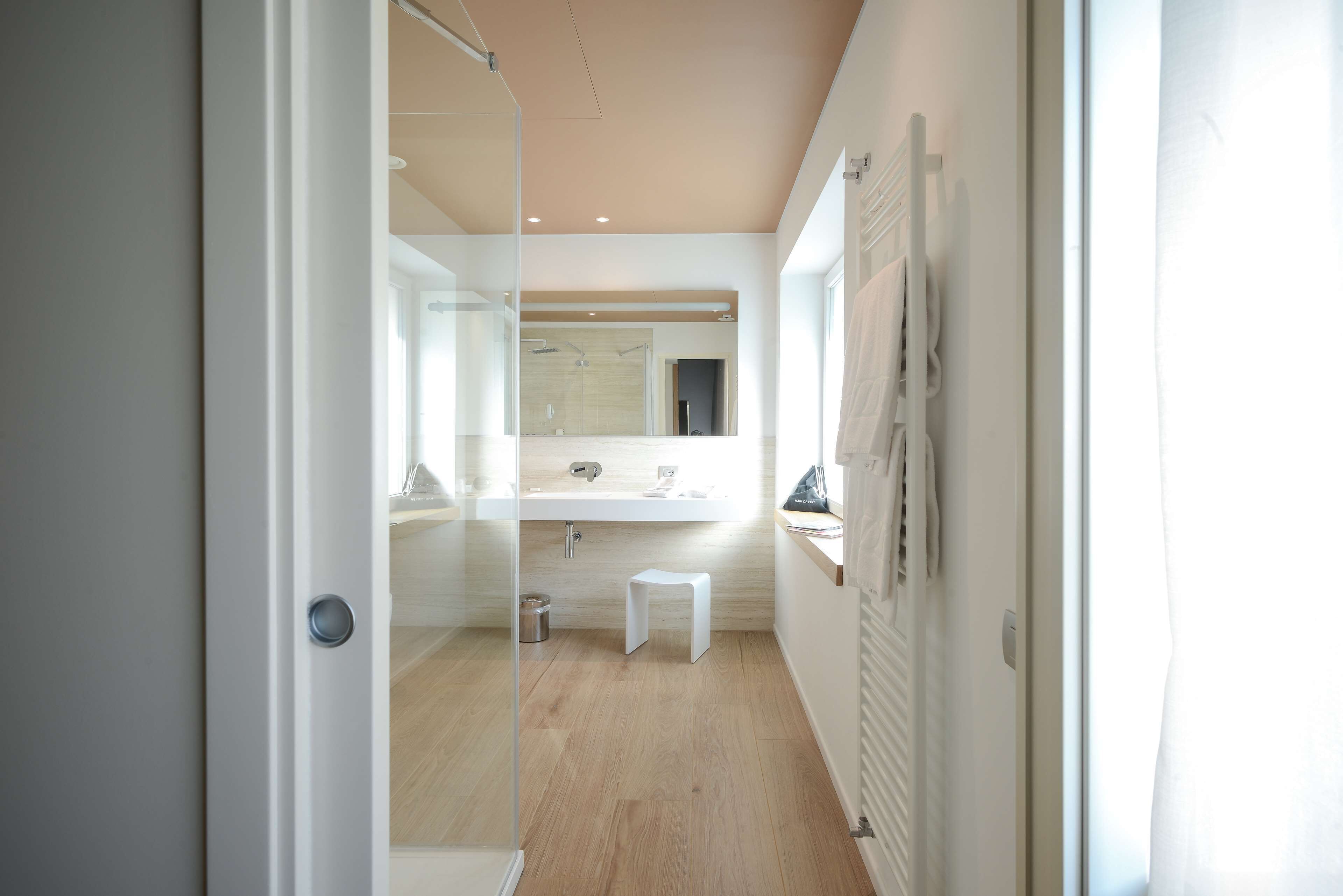 Un baño moderno con separador de vidrio, un lavabo blanco y un taburete pequeño.
