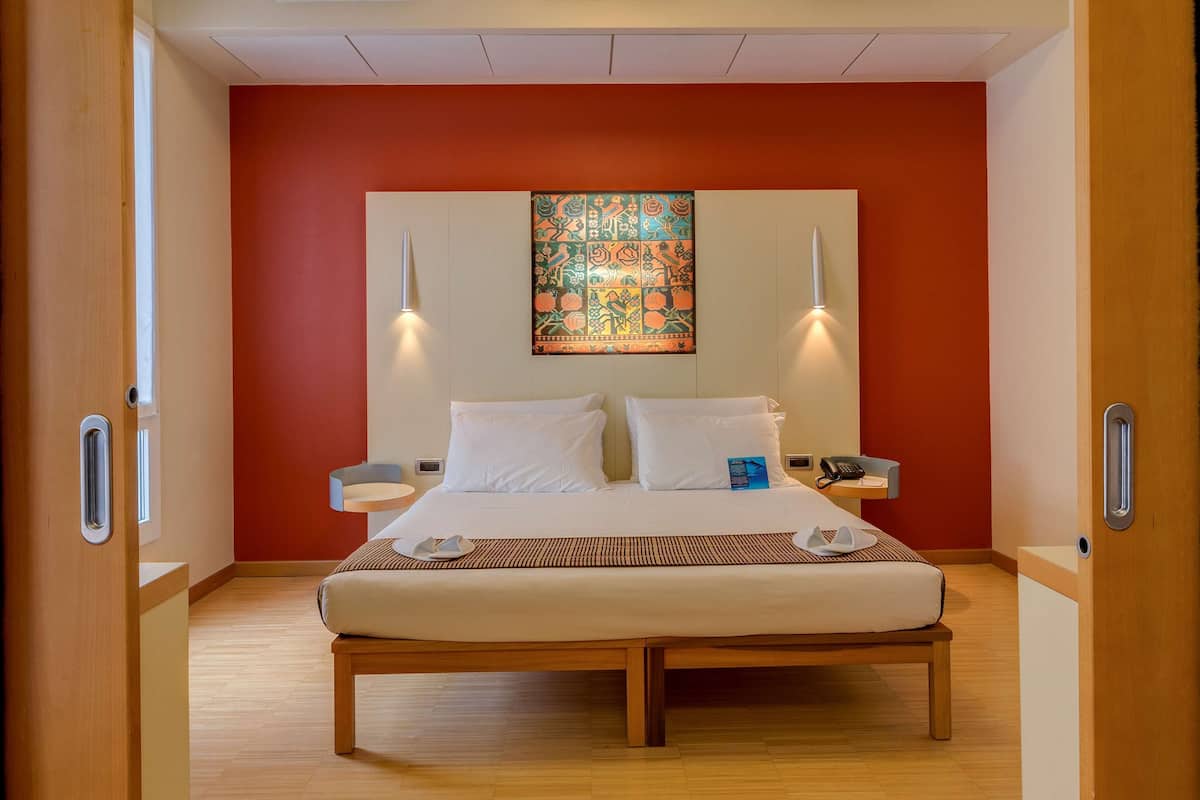 Una camera d'albergo con un letto, due comodini, un quadro appeso al muro e un telefono.