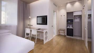 A modern hotel room with a bed, desk, chair, TV, and a walk-in closet with shelves and a drying rack.