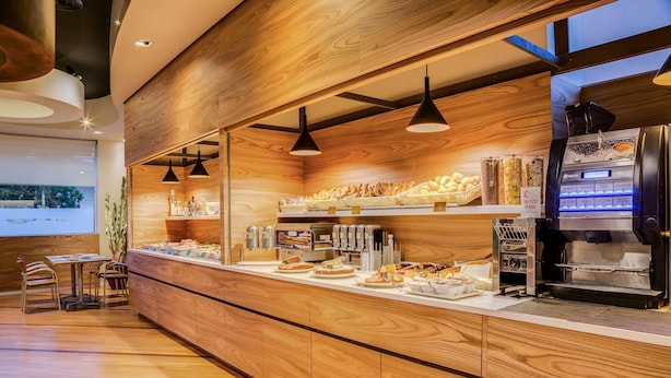 A bakery counter with various baked goods, a coffee machine, and seating area with tables and chairs. - Best Western Plus Hotel Bologna (Mestre)