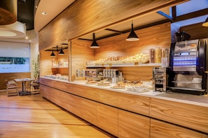 Mostrador de panadería con diversos productos horneados, una máquina de café y una zona de estar con mesas y sillas.
