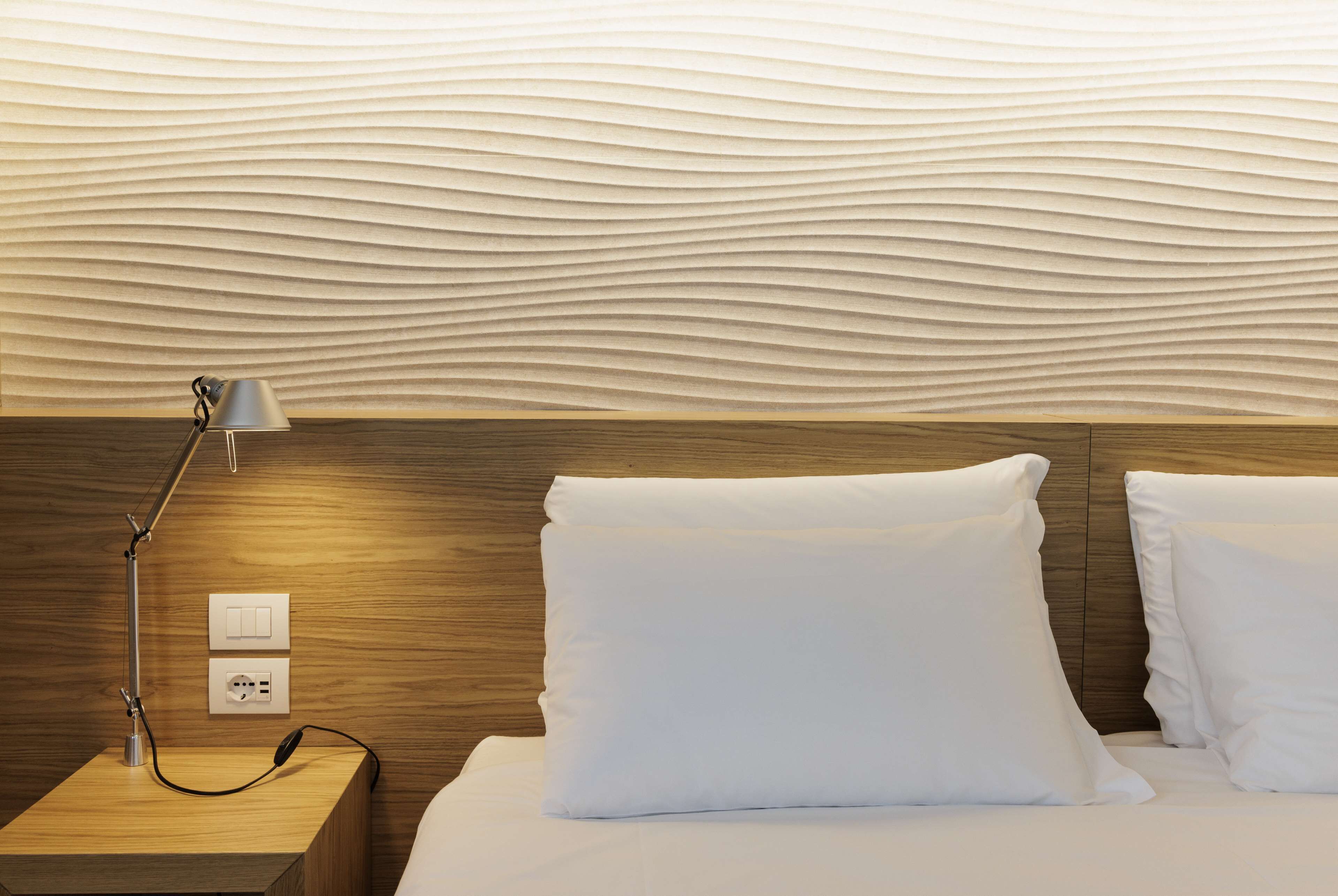 A neatly made bed with white pillows, a bedside lamp, and a wooden headboard.