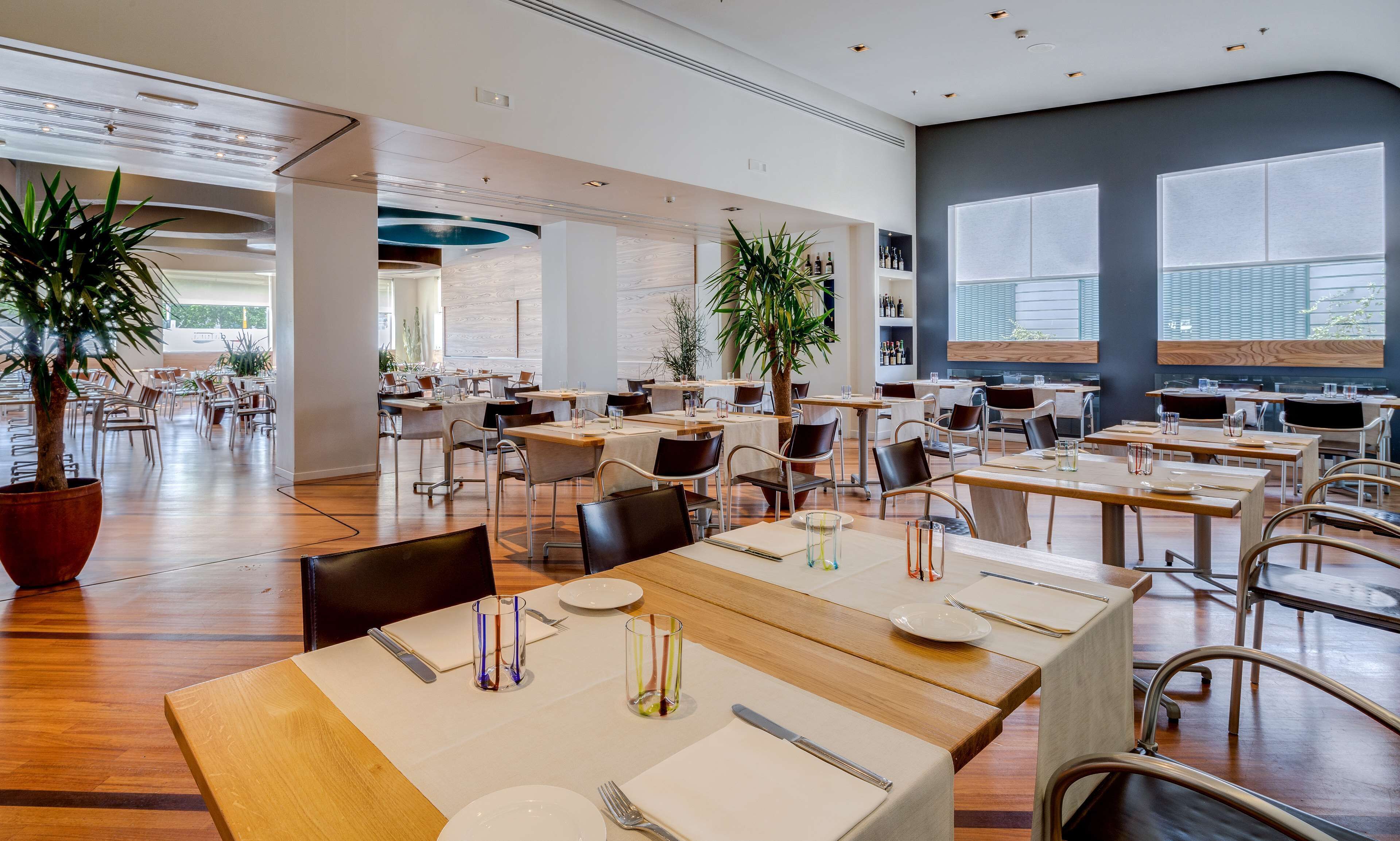 A spacious restaurant with high ceilings, modern furniture, and large windows.