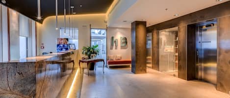 Eine moderne Lobby mit einer Marmor-Rezeption, einer Bank, einer Topfpflanze und einem Aufzug.