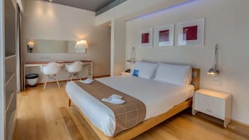 A modern hotel room with a wooden bed, a desk with chairs, a large mirror, and artwork on the wall.