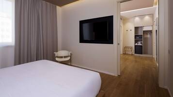 Habitación de hotel con cama, televisión montada en la pared, una silla y suelo de madera.