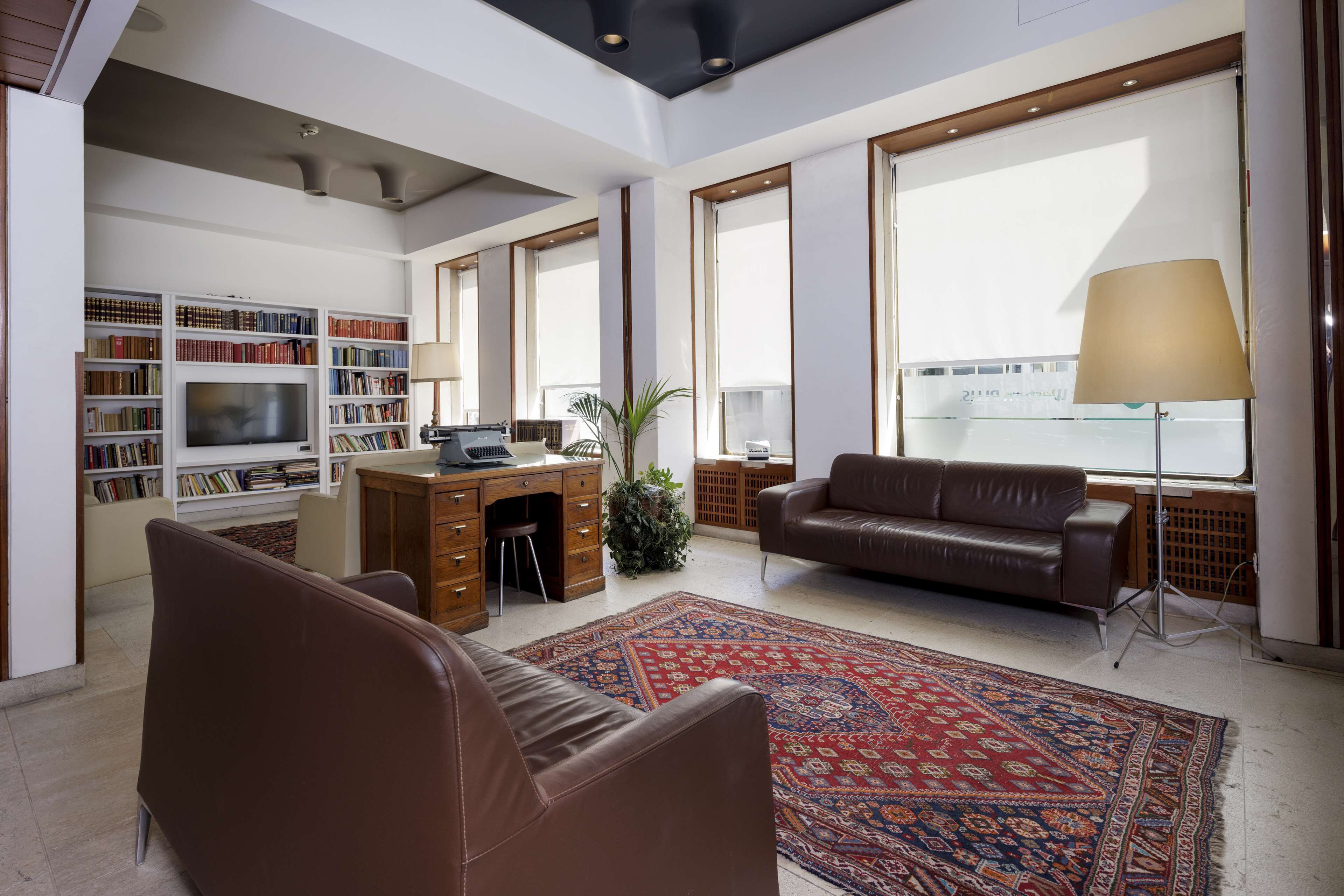 Un salon spacieux avec une grande télévision, un canapé en cuir et un tapis à motifs.