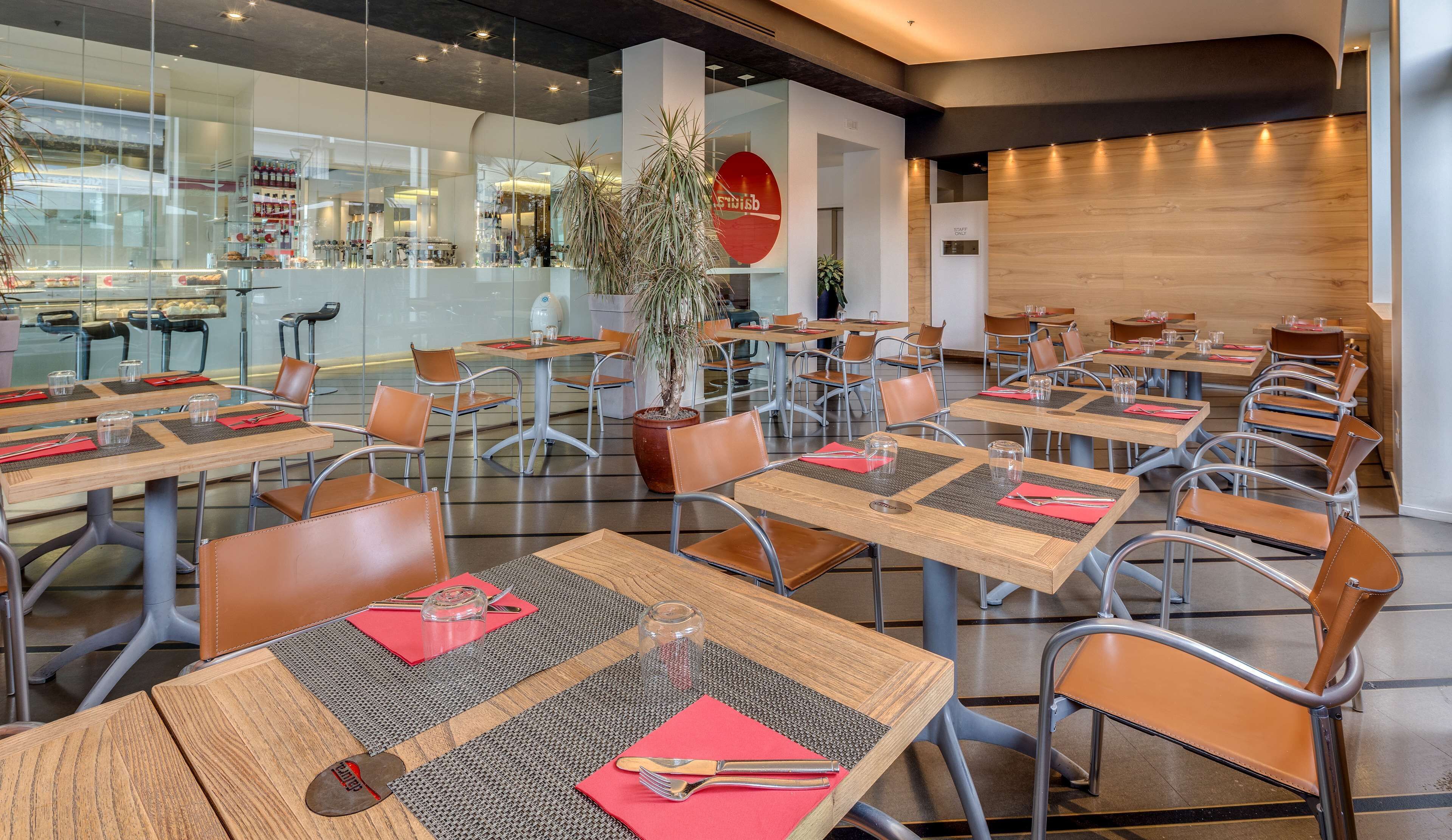A modern restaurant with wooden tables, metal chairs, and red placemats.