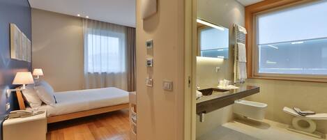 Una habitación de hotel moderna con cama, mesita de noche, lámpara y baño con inodoro y lavabo.