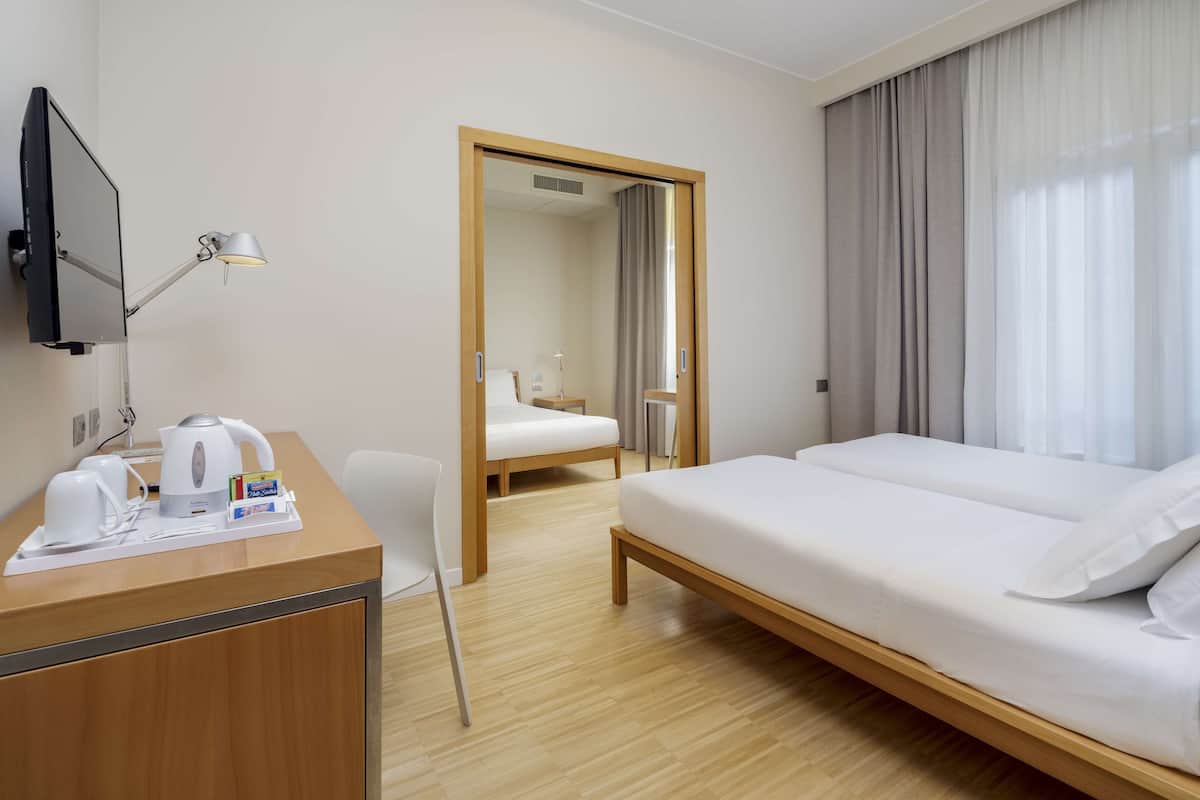 Una camera d'albergo con un letto, una scrivania con lampada, una sedia e una televisione.