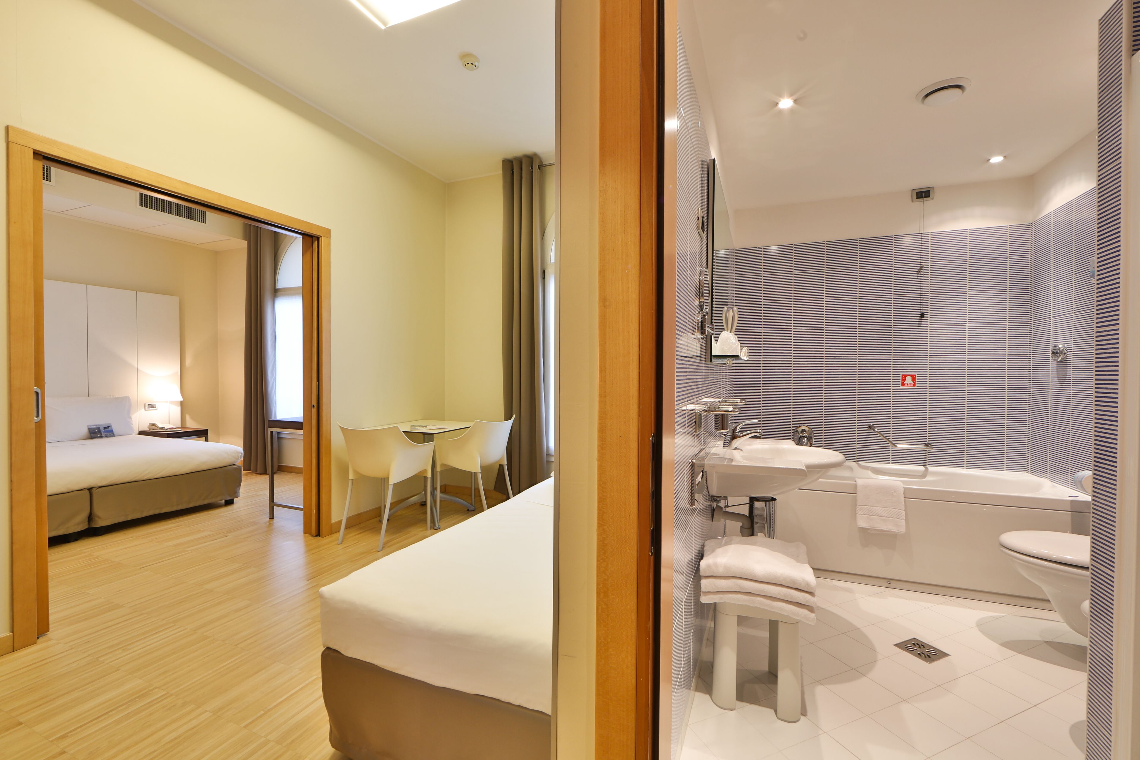 Una habitación de hotel moderna con cama, escritorio y baño con bañera y lavamanos.