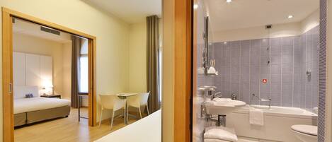 A modern hotel room with a bed, a desk, and a bathroom with a bathtub and sink.