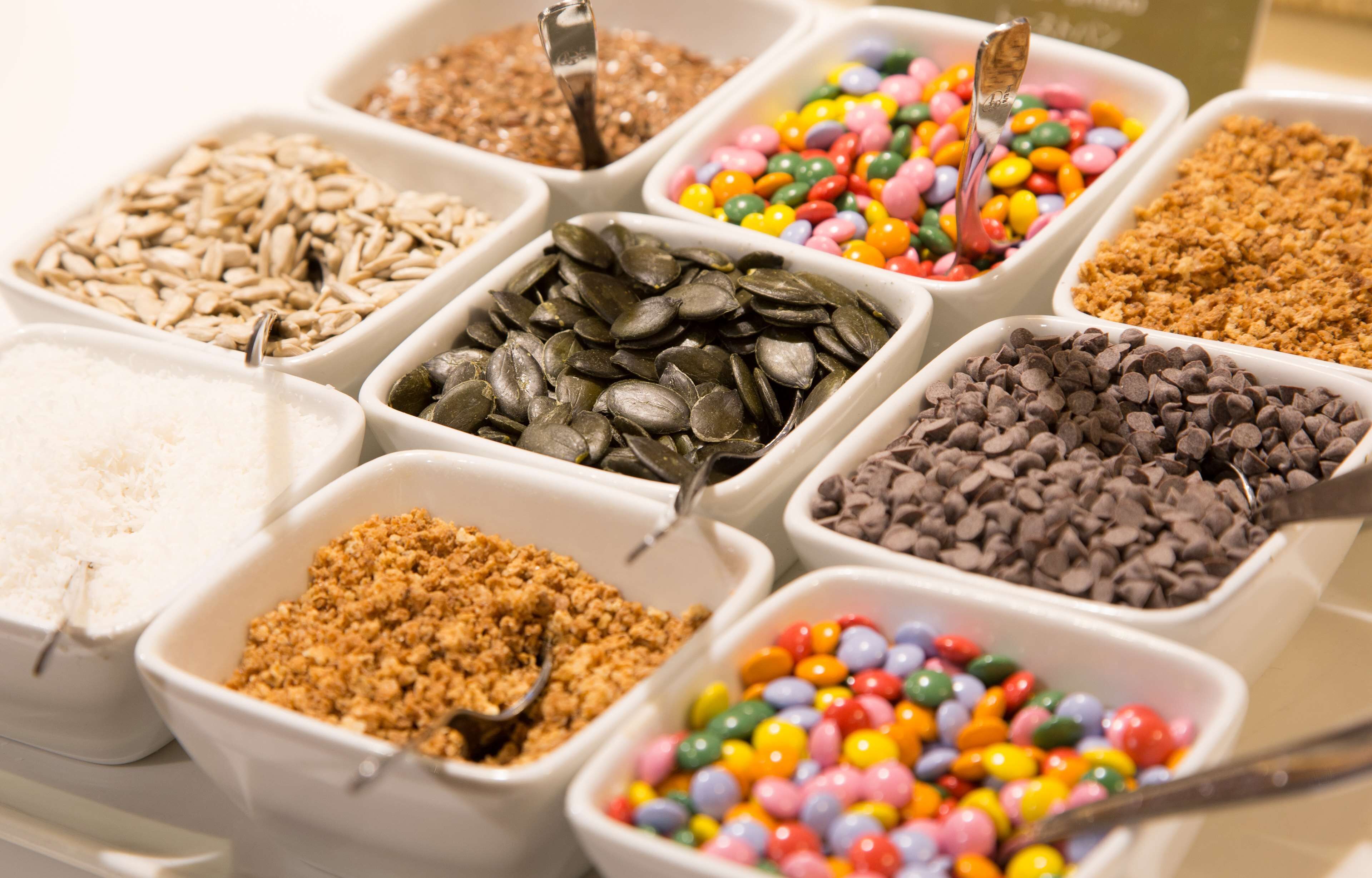 A variety of snack options in white containers, including sunflower seeds, chocolate chips, and colorful candies.