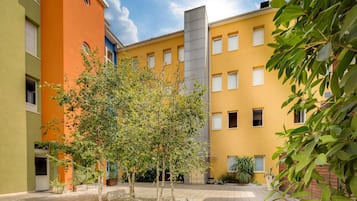 Um pátio com uma árvore, plantas em vasos e um edifício com várias janelas e varandas.