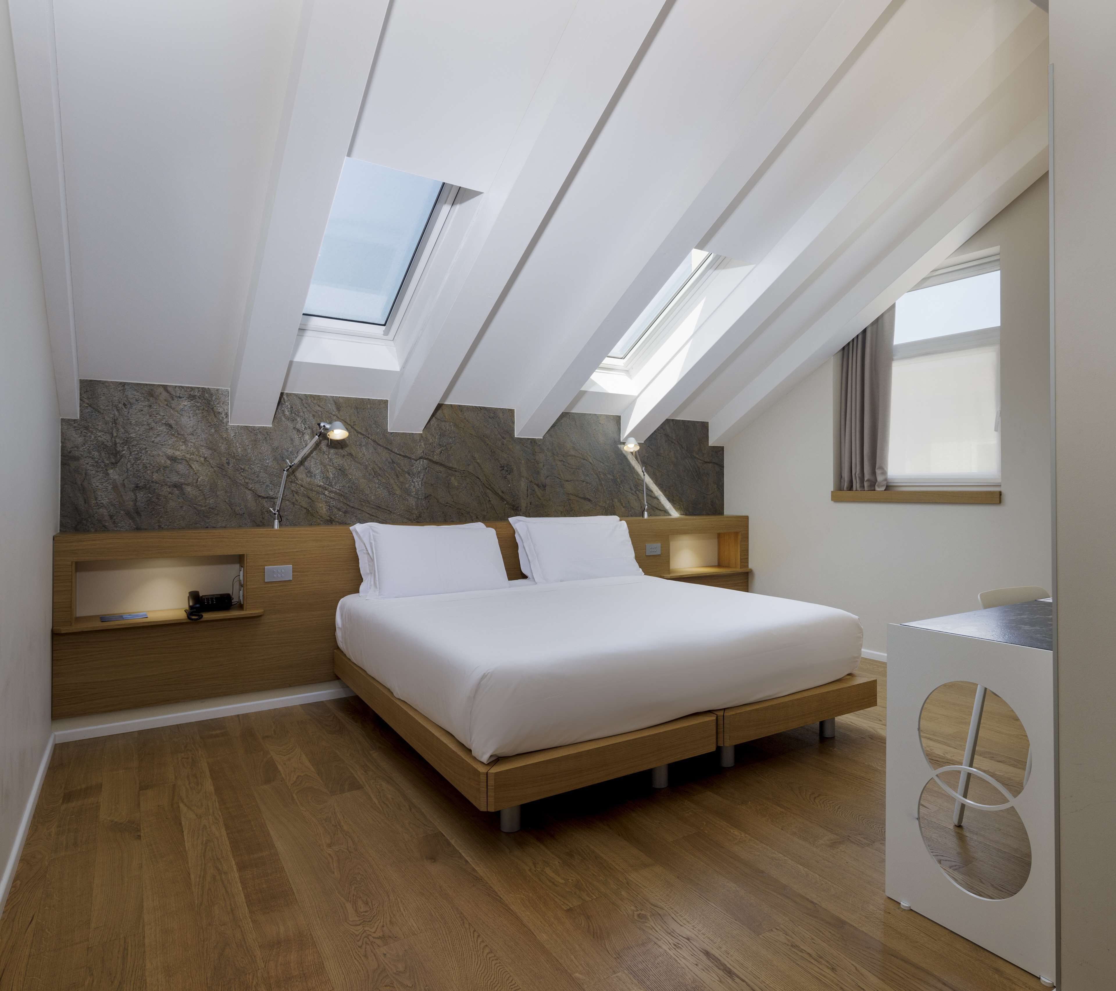 A modern bedroom with a skylight, wooden flooring, a bed, bedside tables, and a desk.