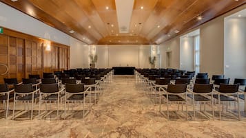 Ein Konferenzraum mit Reihen von Stühlen, einer Bühne und einer Holzbalkendecke.