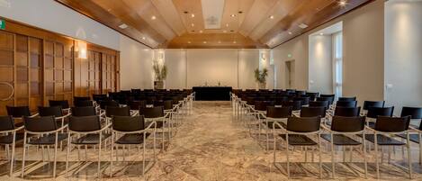 Un salón de conferencias con filas de sillas, un escenario y un techo de madera.
