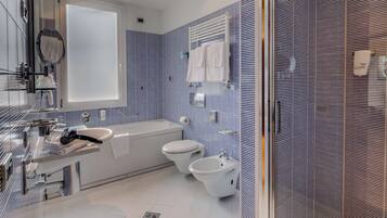 Un baño moderno con un espejo grande, una bañera, dos inodoros y un bidé.