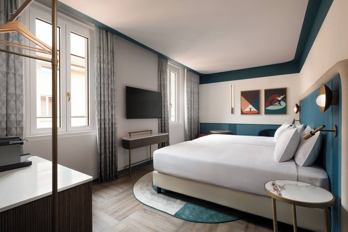 A modern hotel room with a large bed, a desk, a flat-screen TV, and artwork on the walls.