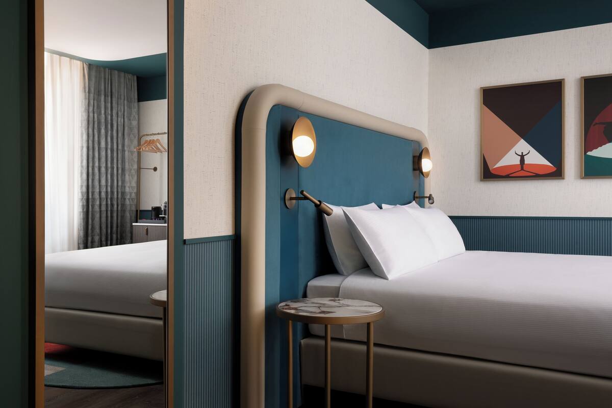 A modern hotel room with a large bed, a bedside table, and a mirror.