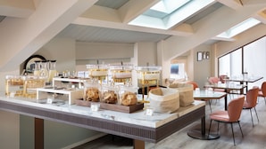 A breakfast buffet with various food items and beverages, a seating area with tables and chairs, and skylights on the ceiling. - Puccini Hotel Milan, Tapestry Collection by Hilton (Milan)