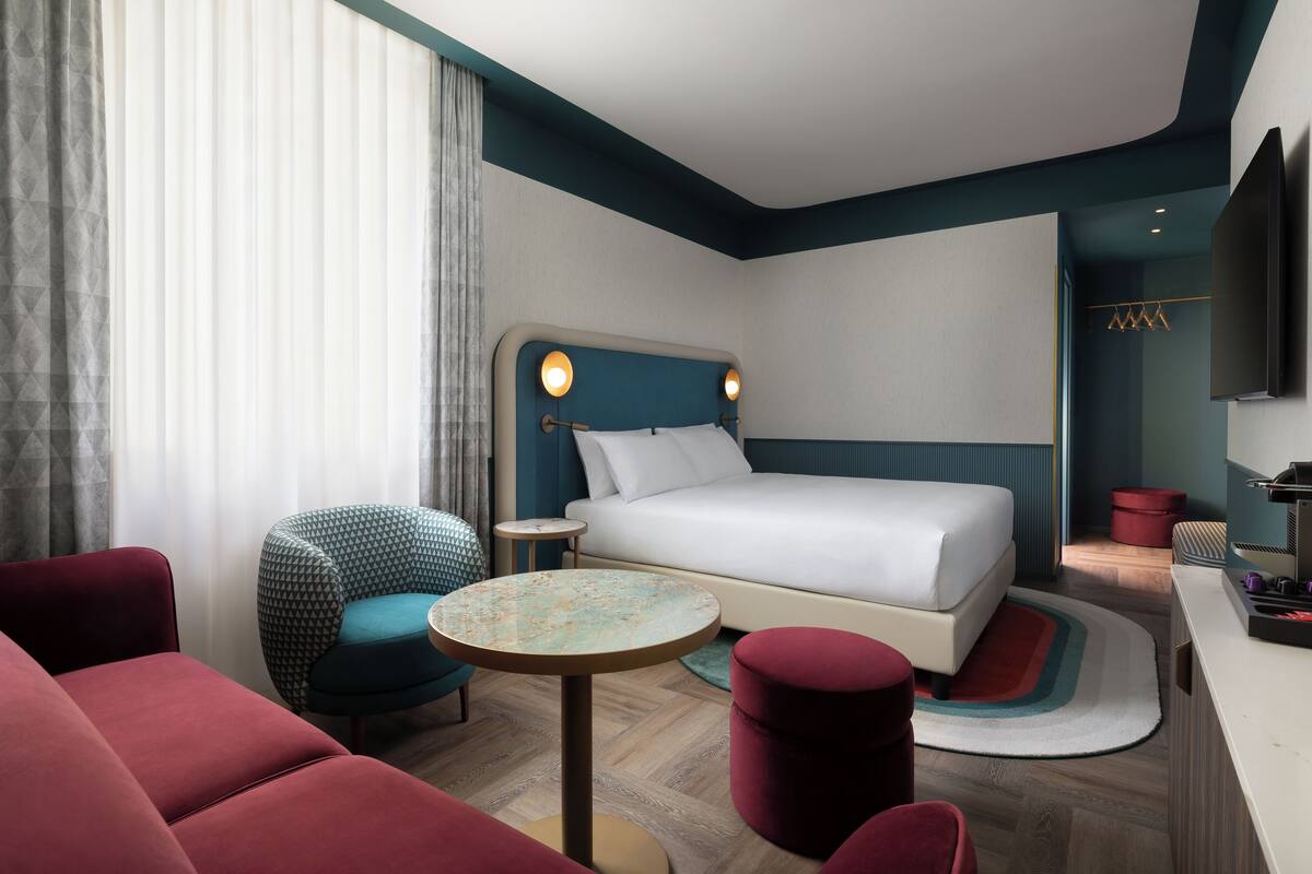 A modern hotel room with a bed, a round table, a chair, and a TV.