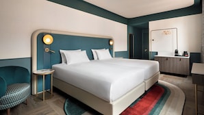 A modern hotel room with a large bed, bedside tables, a small round table, and a desk with a mirror. - Puccini Hotel Milan, Tapestry Collection by Hilton (Milan)