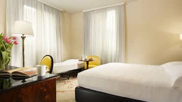 A hotel room with a large bed, a desk with a lamp, a chair, and a small table with a cup and a book.