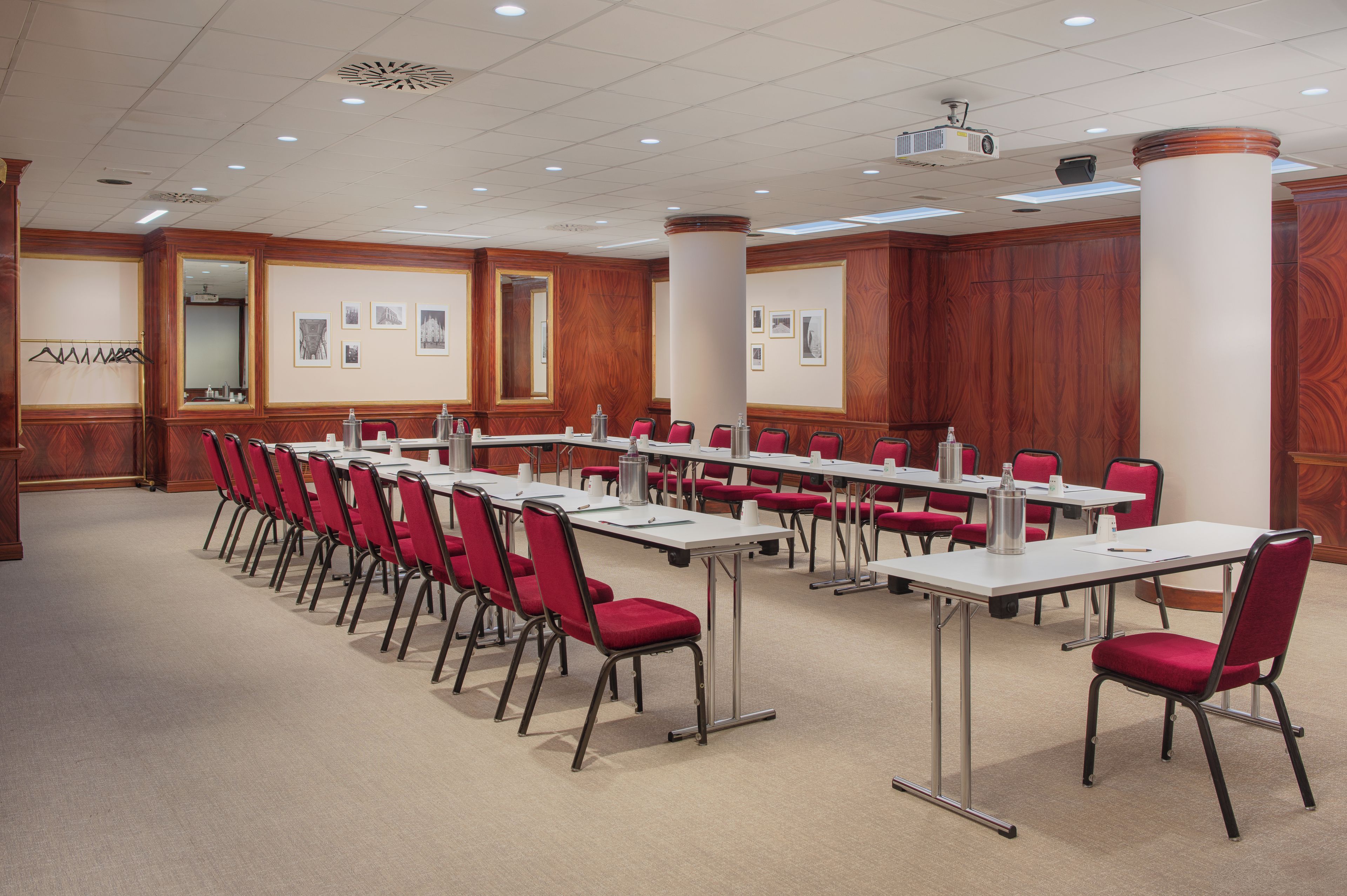 Ein Konferenzraum mit langen Tischen und roten Stühlen, ausgestattet mit Projektoren und einem Teppichboden.