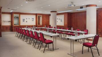 Une salle de conférence dotée de longues tables et de chaises rouges, équipée de projecteurs et recouverte d’un tapis.