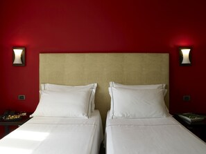 Habitació d'hotel amb dos llits, una paret vermella i làmpades subjectes a la paret.