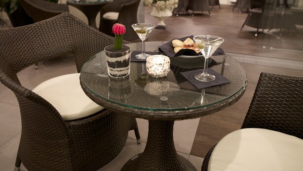 A glass table with a cactus, martini glasses, and a small bowl of pastries in a hotel lobby. - Hotel Montini (Peschiera Borromeo)