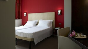 A hotel room with a large bed, two bedside tables, a chair, and a nightstand with a lamp. - Hotel Montini (Peschiera Borromeo)
