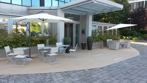 An outdoor seating area with tables and chairs, umbrellas, and potted plants. - Hotel Montini (Peschiera Borromeo)