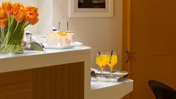 A modern bar area with a white counter, a framed cityscape picture, and a vase of orange tulips. - UNA Hotels Mediterraneo Milano (Milan)