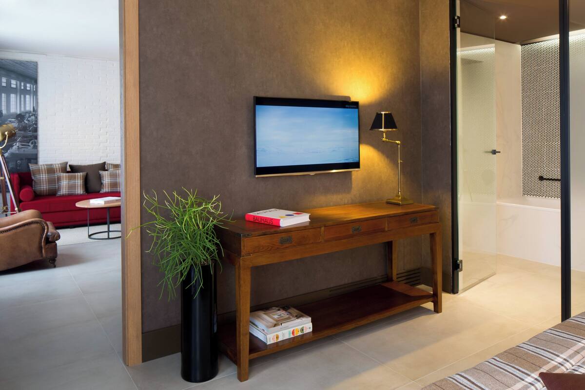 A modern living room with a TV mounted on a wall, a wooden console table with books, a potted plant, and a red sofa.