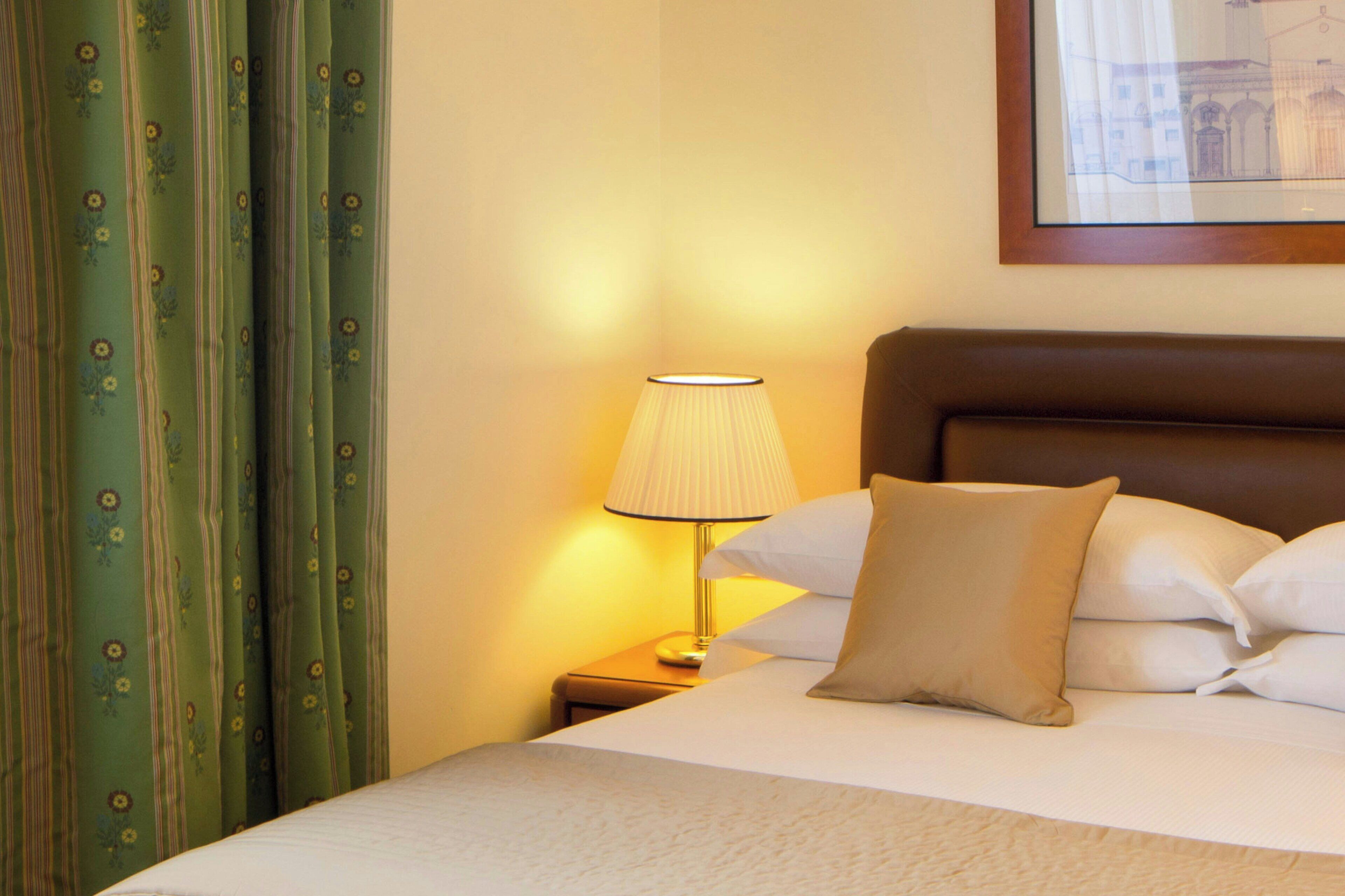 Een hotelkamer met een bed, kussens, een lamp en gordijnen.