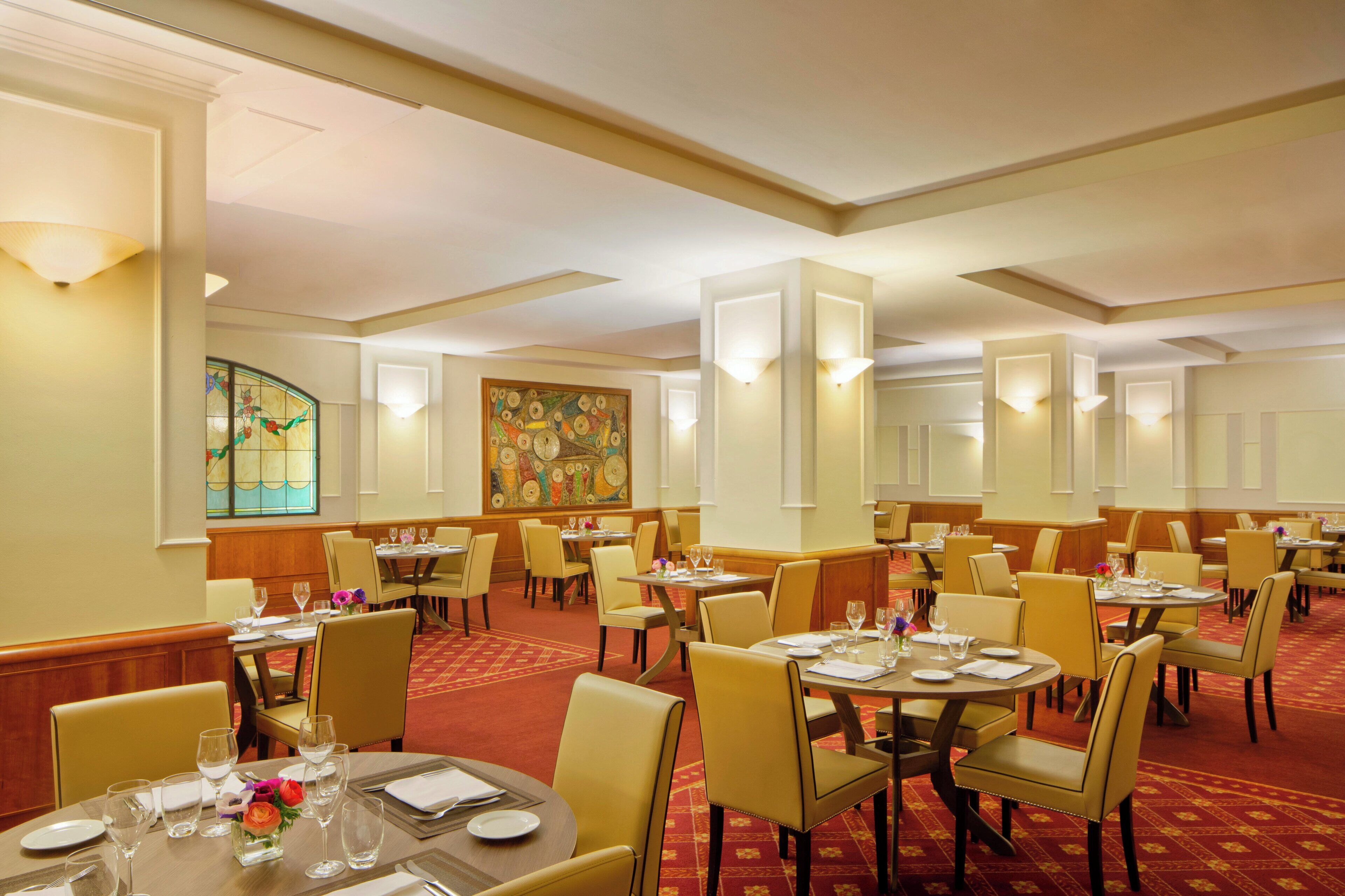Een restaurantgedeelte in een hotel met ronde tafels, stoelen en een vloerkleed.
