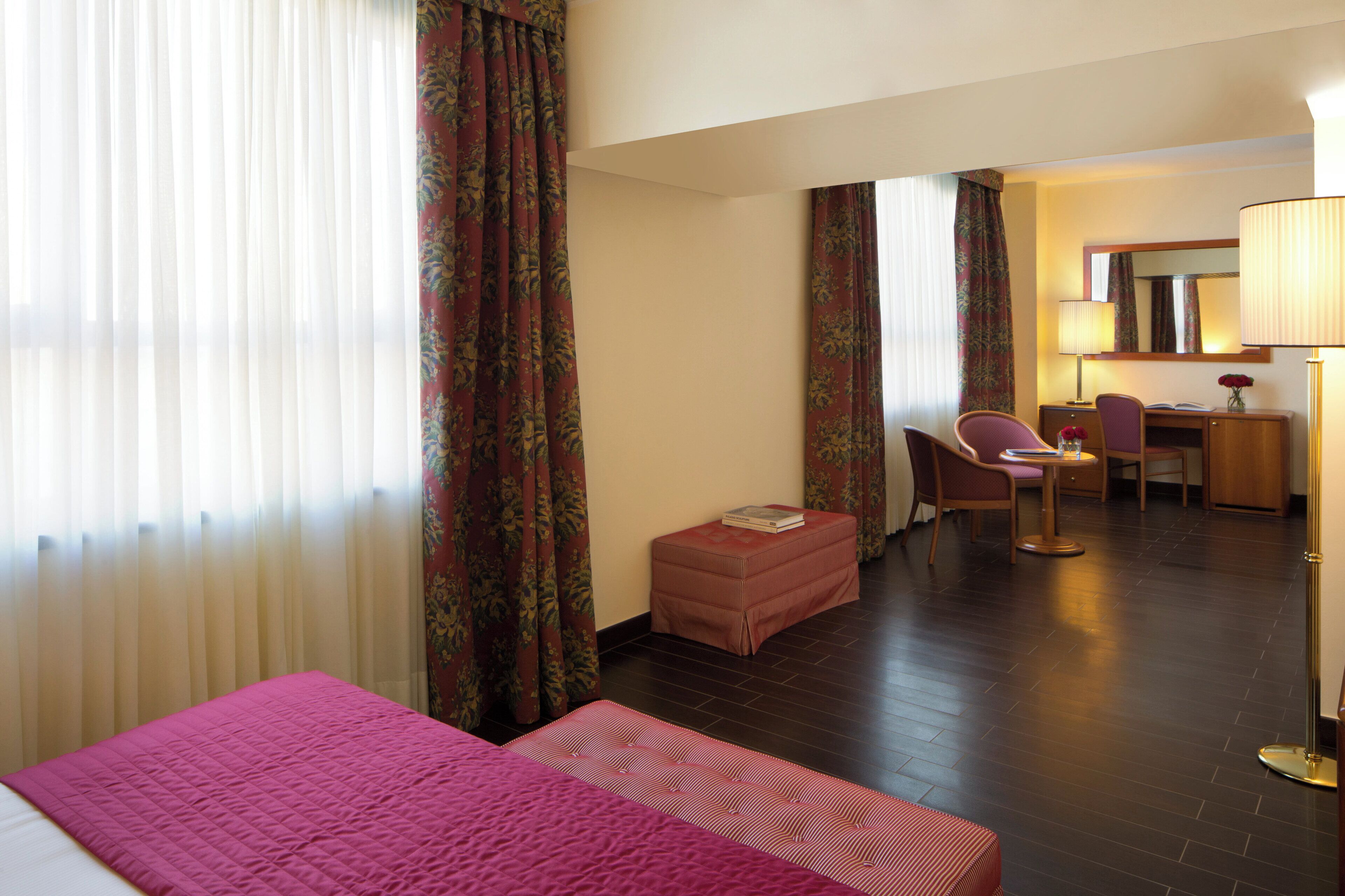 A hotel room with a bed, a desk, a chair, and a small table.