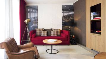 Ein modernes Wohnzimmer mit einem roten Sofa, einem Ledersessel, einem runden Couchtisch und einem Bücherregal.