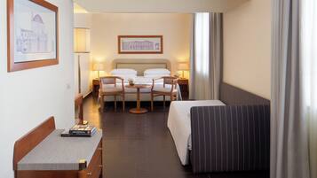 A hotel room with a bed, two chairs, a small table, a nightstand, and a lamp.