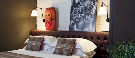 Una cama bien tendida con ropa de cama escocesa, dos lámparas fijadas a la pared y una fotografía grande en blanco y negro.