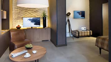 Quarto de hotel moderno com parede de pedra, televisão grande, sofá, mesa de centro e cama.