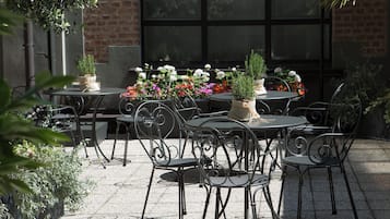 An outdoor patio with round tables and metal chairs, surrounded by potted plants and flowers.