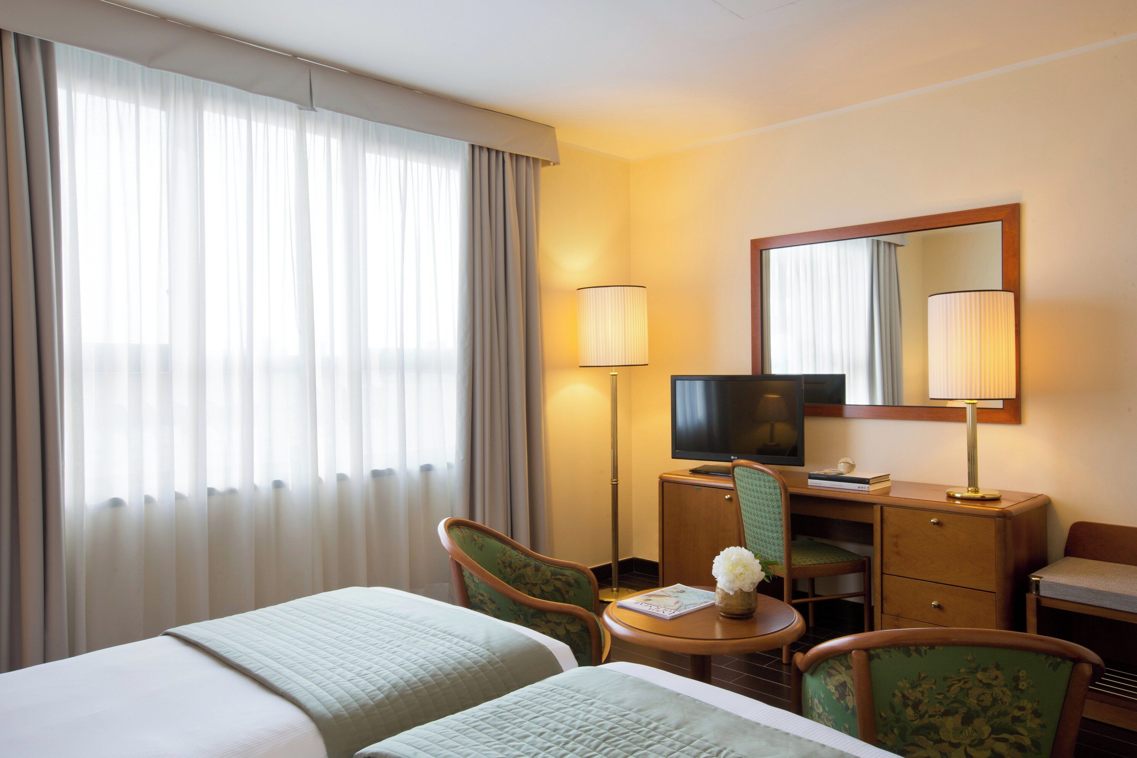 Une chambre d’hôtel avec deux lits, un bureau équipé d’une télévision, d’une lampe et d’une chaise.