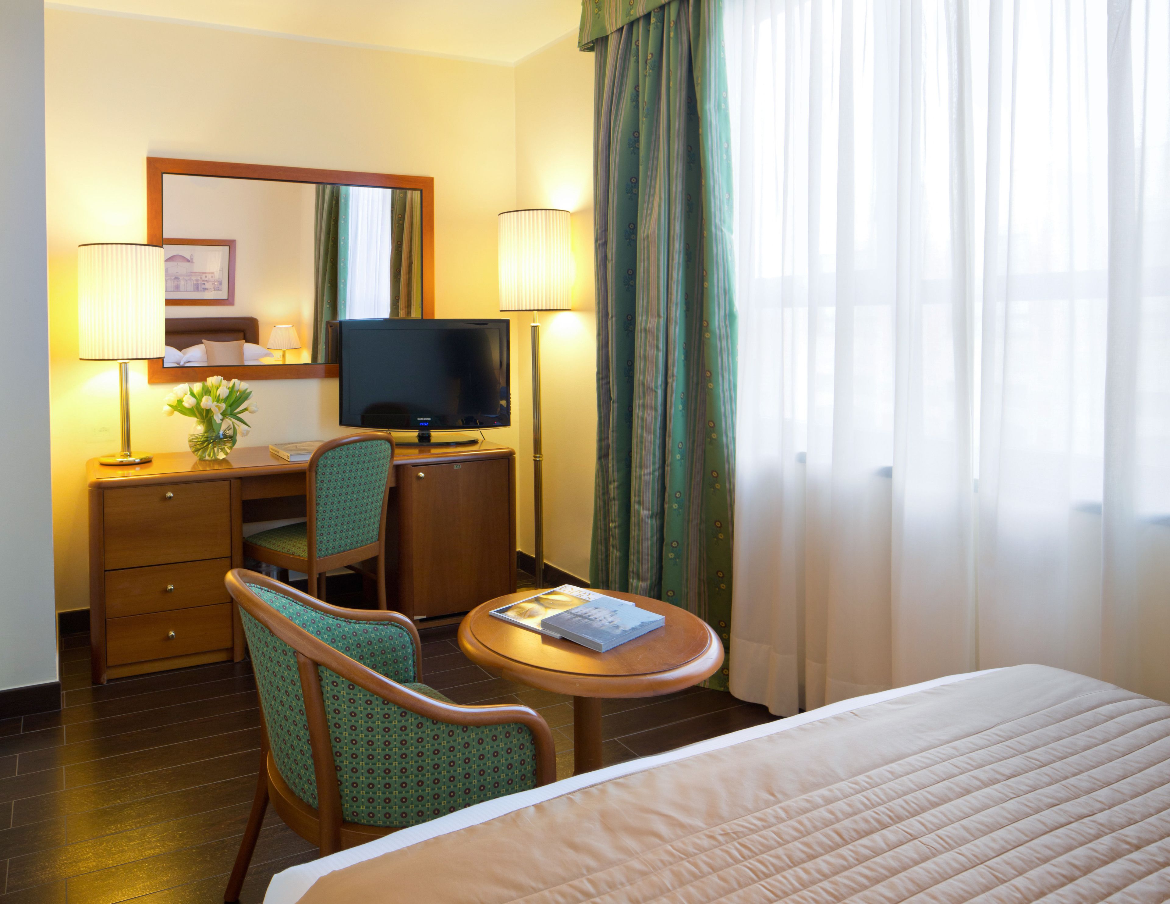 Een hotelkamer met een bed, een bureau met een computer, een stoel, een televisie en een lamp.