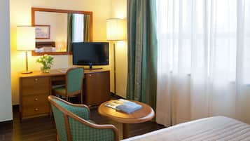 Een hotelkamer met een bed, een bureau met een computer, een stoel, een televisie en een lamp.