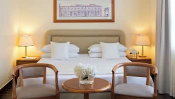 Habitación de hotel con una cama grande, dos lámparas de noche, un cuadro enmarcado en la pared y una pequeña mesa con sillas.