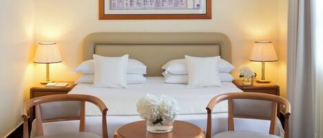 A hotel room with a large bed, two bedside lamps, a framed picture on the wall, and a small table with chairs.